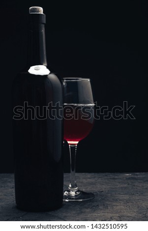 Bottle of red wine and wineglass on a dark wooden table black background behaid.
