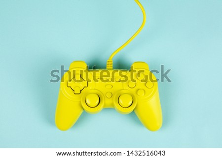 a yellow painted video game controller on a plain turquoise background. Minimal color still life photography