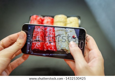 A girl photographs red and white sushi on the phone from different angles. Photo close up.