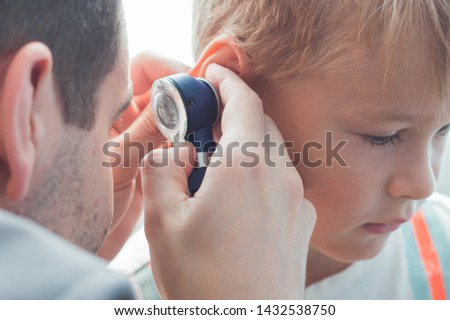 A child with otitis at the reception at the children's otolaryngologist in the hospital. Cute boy with bad ears at the doctor's office in the clinic. Royalty-Free Stock Photo #1432538750