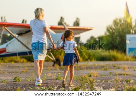 Back view of cheerful mother and daughter smiling plane while spending time in green field together