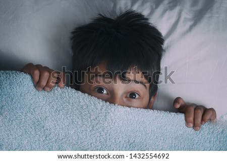 the boy lies on a bed the top view hid under a blanket for fear
