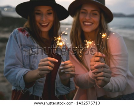 Two best friends celebrating, holding sparklers at beach 