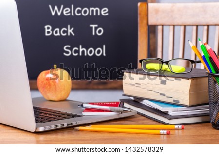 Closeup of laptop computer and stack of books on a desk with Back To School written on blackboard in background