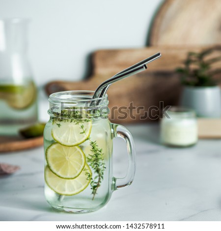 Cold drink in mason jar with metal straws on kitchen table. Lemonade or detox water with lime and thyme in glass jar wit metal straw indoor. Recyclable straws, zero waste concept Royalty-Free Stock Photo #1432578911