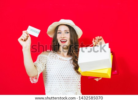 Portrait of a smiling cheerful girl holding shopping bags and showing credit card over red background