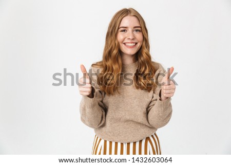 Beautiful cheerful young girl with long blond curly hair wearing sweater standing isolated over white background, thumbs up
