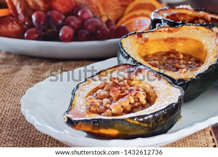 Baked acorn squash with walnuts served for Thanksgiving Day dinner with roast stuffed turkey blurred in background. 