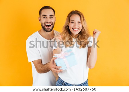 Image of smiling couple rejoicing while handsome man giving present box to beautiful woman isolated over yellow background