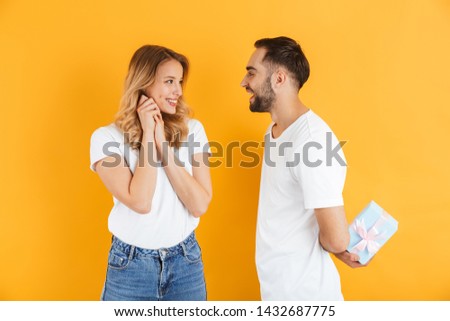 Image of happy couple rejoicing while handsome man giving present box to beautiful woman isolated over yellow background