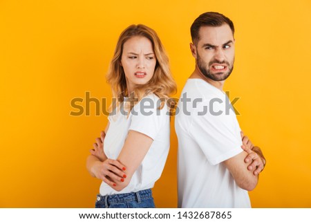Image of angry people man and woman in basic t-shirts frowning while standing back to back during fight isolated over yellow background