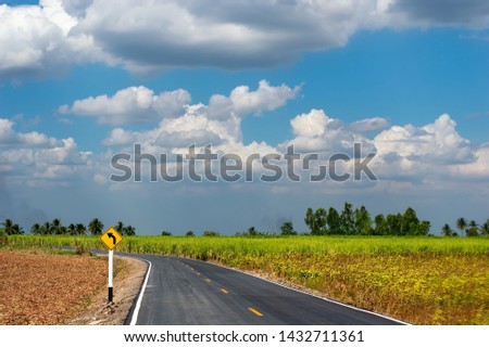Yellow road sign on a rural road warning of a left-hand bend through Sugarcane farm with blue sky and cloud