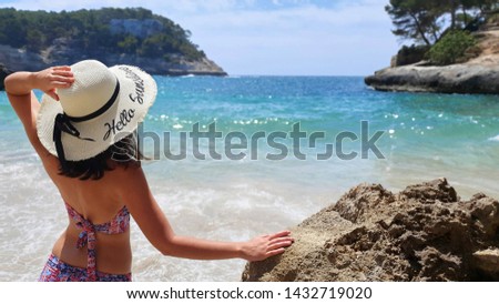 Woman on her back on the beach with turquoise waters on her back with a hat with the inscription hello sunshine on the seashore in summer.