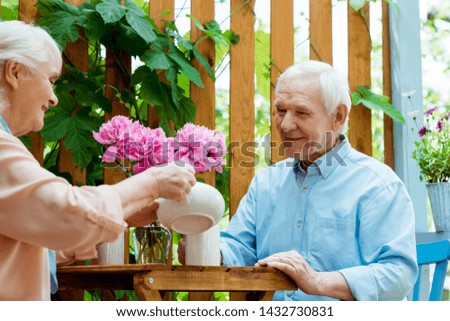 low angle view of cheerful senior woman holding teapot near cup and happy husband 