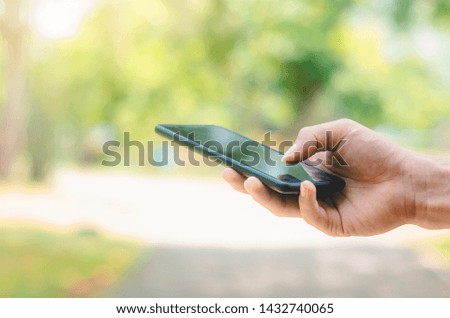 close up handsome man use hand typing mobile phones and touch screen working search with app devices in park with sunrise and green blur nature background.
