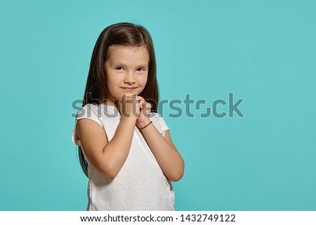 Close-up shot of a cute brunette little girl in a white blouse posing against a blue background.