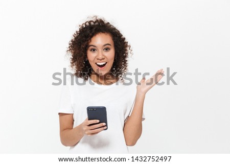 Portrait of a pretty cheerful casual african girl standing isolated over white background, using mobile phone