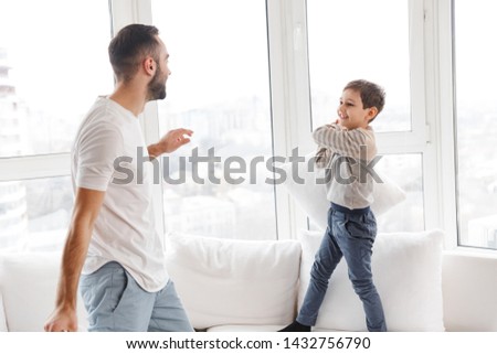 Picture of Cheerful bearded father and his young son having fun with pillows at home