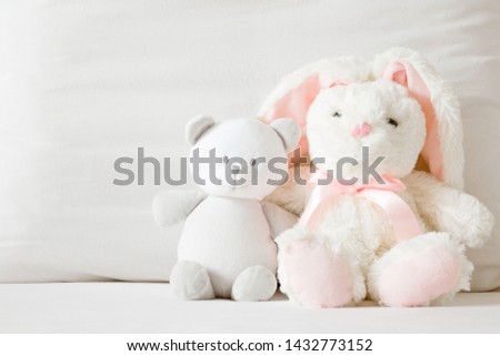 Smiling white teddy bear and fluffy bunny sitting on bed at pillow. Togetherness and friendship concept. Kids best friends. Front view. Closeup.