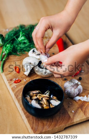 Photo of a preparation of ingridients such as musseles, red chilli peppers, fresh greens, mushrooms, broccoli with attractive woman hands on a wooden table