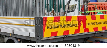 White open bed truck with yellow and red diagonal Highway Maintenance signage is stacked with metal and orange plastic road closure, event crowd control or diversion barriers. 