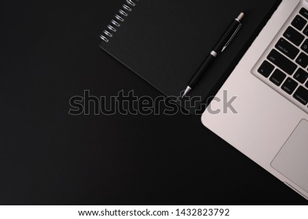 Flat lay, top view of black spiral notebook ,pen, and laptop on black desk,business office desk minimal style. with copy space for your text