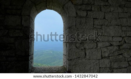 stone wall and arched window openings with a view of a mountain range with forest and haze over the mountains
