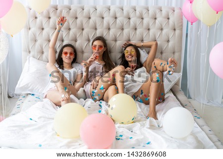 Pajama party. Attractive young smiling women in pajamas drinking champagne while having a slumber party in the bedroom
