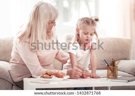 Time for drawing. Smiling grandmother feeling good while drawing pictures with her granddaughter