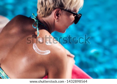 Woman with sun protection crem on her back in shape of smile sitting on the pool. People, summer, vacation and healthcare concept