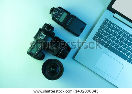 Equipment of professional photographer. Laptop, camera, lenses and flash. Holographic blue light. Top view