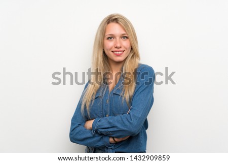 Young blonde woman over isolated white wall with arms crossed and looking forward