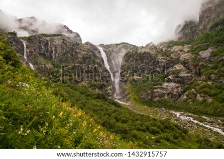 Cascade waterfalls in the clouds and yellow wildflowers after the rain