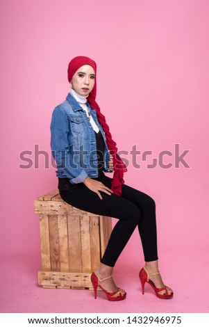 Fashionable female model in black pants, long sleeves jeans jacket and hijab isolated on pink background. Stylish Muslim female hijab fashion lifestyle portraiture concept.