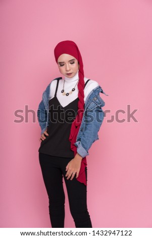 Fashionable female model in black pants, long sleeves jeans jacket and hijab isolated on pink background. Stylish Muslim female hijab fashion lifestyle portraiture concept.