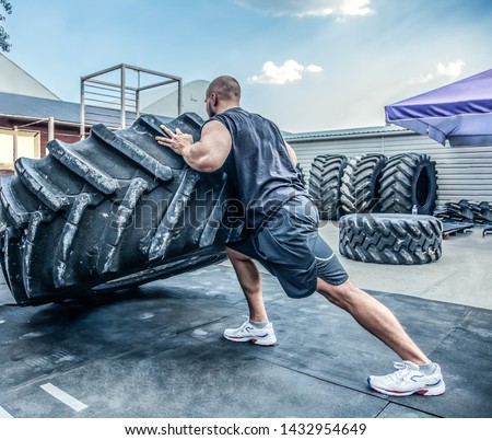 back view of strong muscular fitness man moving large tire in street gym. Concept lifting, workout training. Royalty-Free Stock Photo #1432954649
