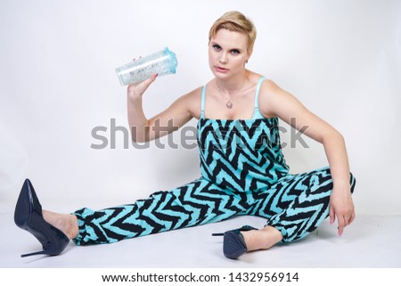 charming plus size young woman in black blue jumpsuit with glass of water on white background in Studio. pretty blonde girl wearing fashion city style overall and posing.
