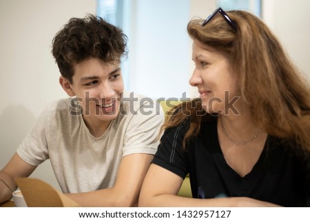 The teenager communicates with his mom in the cafe and smiles. He enthusiastically tells something to mom. Mom looks at her son with love and does not believe that he grew so fast. Focus on the boy Royalty-Free Stock Photo #1432957127
