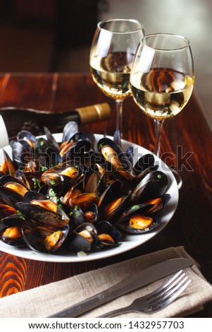 Fine dining in a seafood restaurant: a big dish of mussels with bottle of white wine with two wine glasses, on dark background  Royalty-Free Stock Photo #1432957703