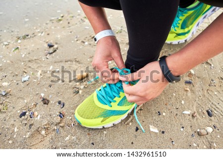 Woman tying running shoe laces preparing for run on ocean beach, copy space, closeup. Female fitness runner getting ready for jogging outdoors