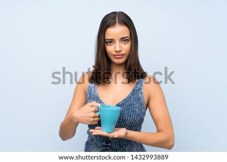 Young woman over isolated blue wall holding hot cup of coffee