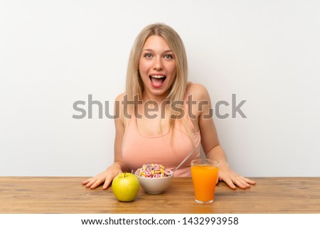 Young blonde woman having breakfast with surprise facial expression