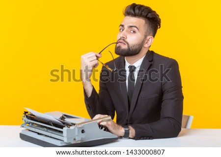 Young pensive business man or manager types a document on a typewriter on a yellow background. Office concept and documentation.