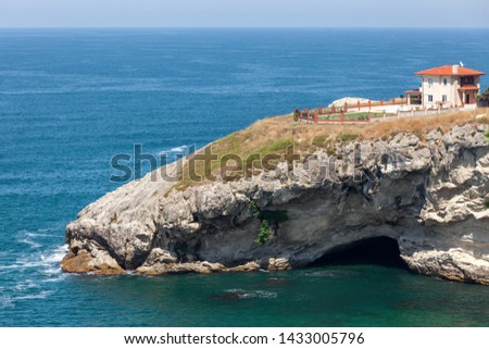 Duplex house with a huge garden is placed on the edge of the cliff. Under the cliff, there is a cave and sea is entering the cave. Ocean view.