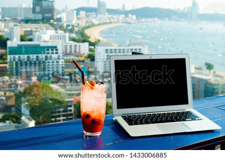 Laptop and glass of summer cocktail on a wooden table, on a bright beautiful panoramic background of the city