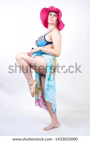 cute girl with curvy figure stands in fuchsia pink hat and blue swimsuit with pareo on white background in Studio. pretty curvy chubby woman in fashionable beachwear posing alone.
