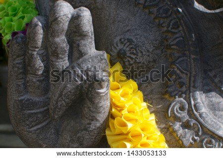 Close up picture of the hand detail of a black Ganesha stone statue decorated with a yellow garland and located in Ubud, Bali - Indonesia