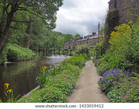 a canal path surrounded by summer flowers with a row of old stone houses at eastwood in hebden bridge west yorkshire Royalty-Free Stock Photo #1433059412
