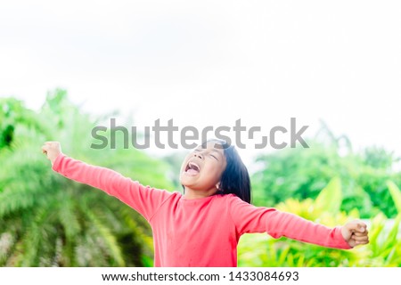 Happy little girl shouting out on the garden.Kid girl singing and raised hands to worship GOD.