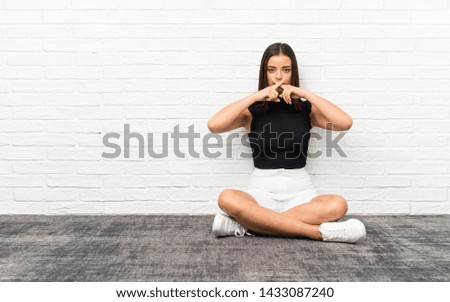Pretty young woman sitting on the floor showing a sign of silence gesture